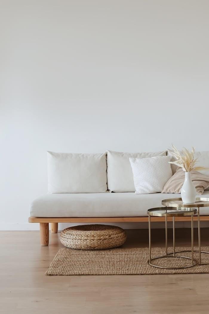about-bg A chic minimalist living room featuring a white sofa with cushions, dried flowers in a vase, and a wooden floor.